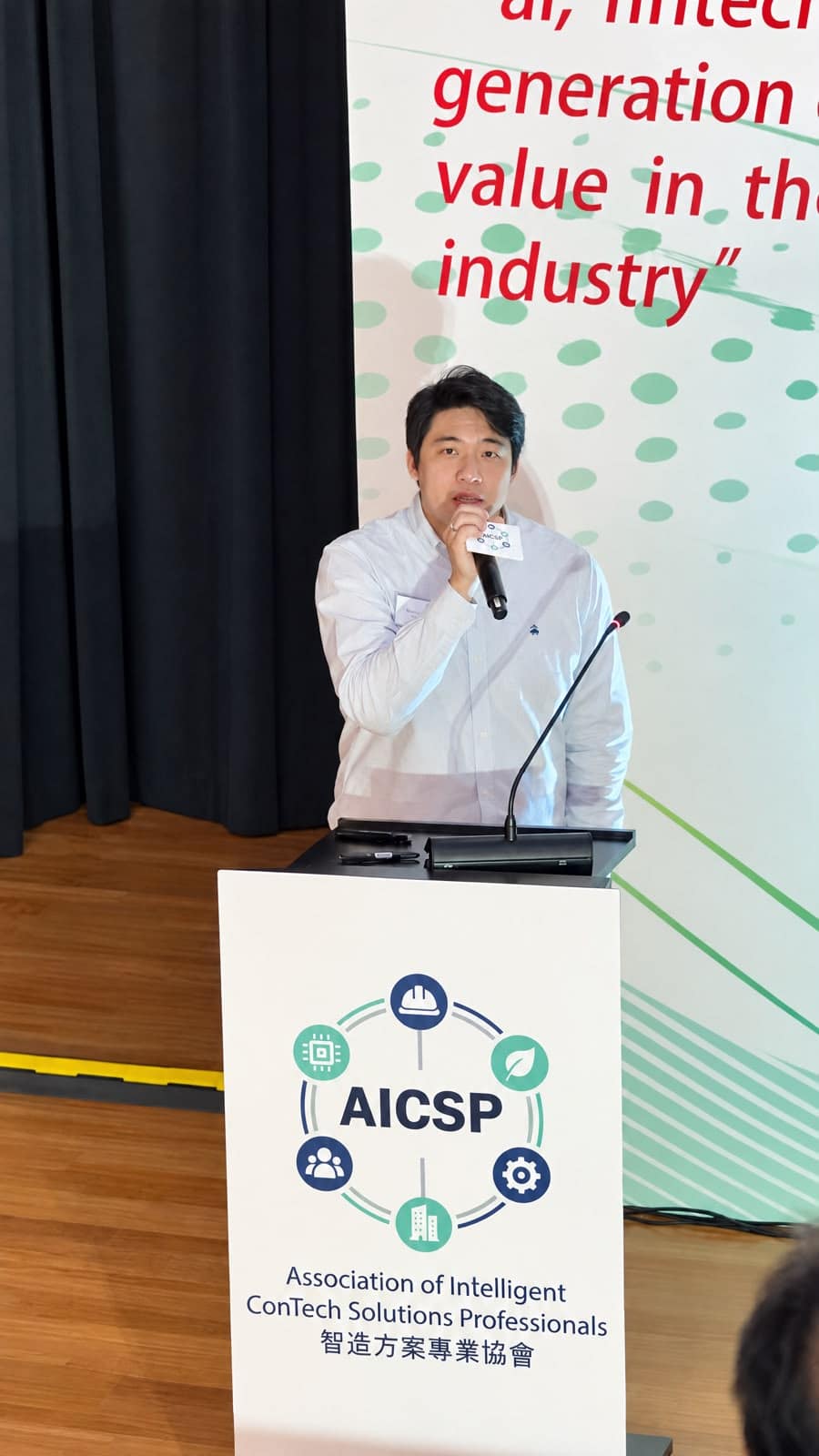 AICSP 活動台上分享場景，講者手持咪高峰站在講台後